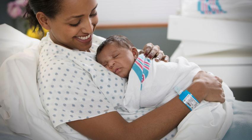 Image of a person holding a newborn baby in a hospital bed