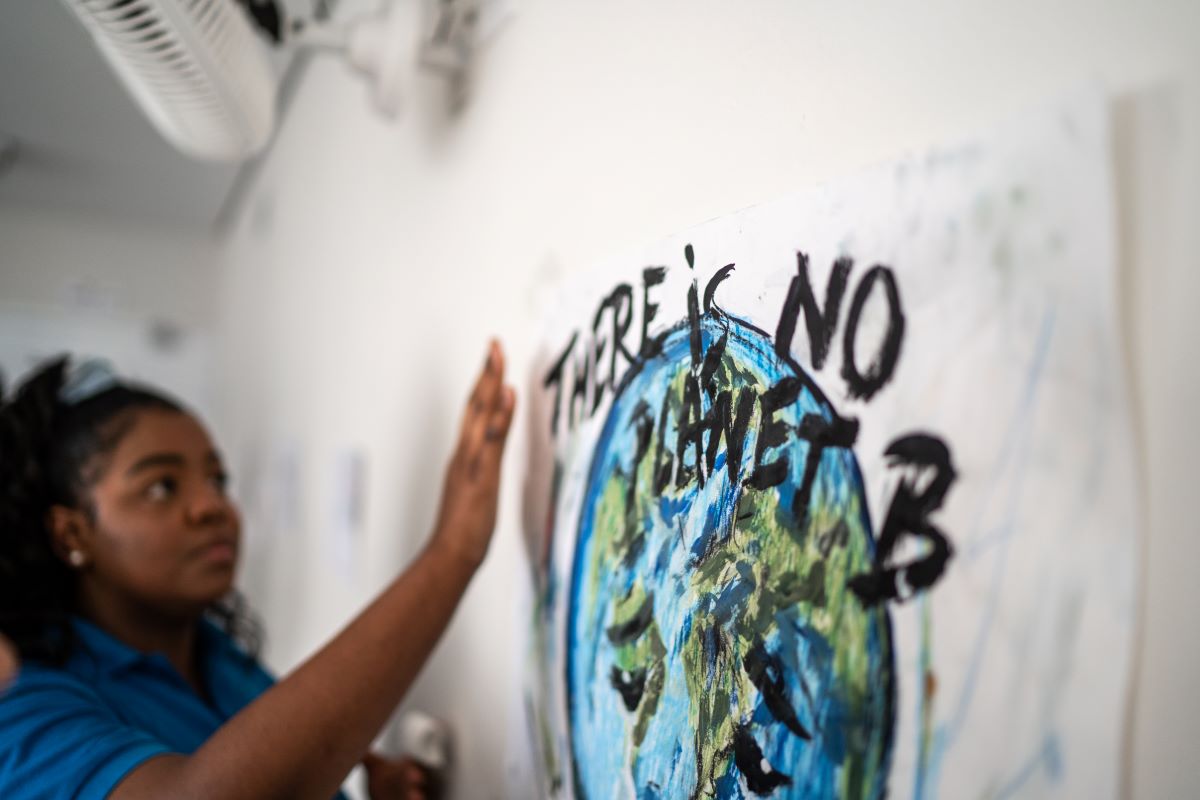 Young Black woman student hangs a poster that says "there is no planet B"