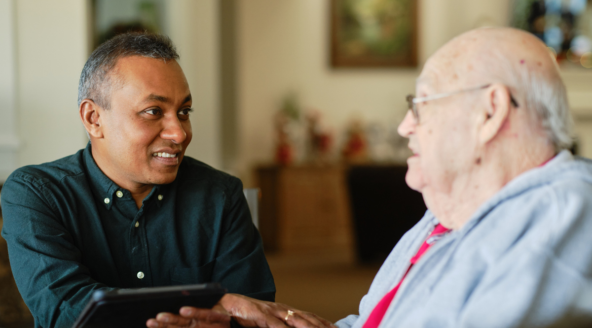 A caregiver holds the hand of an older man he's listening to.