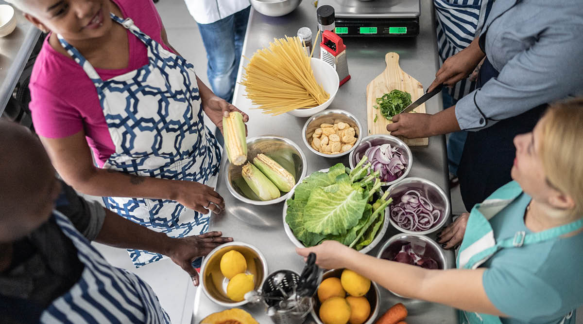 People gather in a kitchen with fresh vegetables during a cooking class.