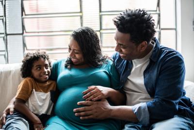 Conception to Cradle 1390901892 A Black mother and father excitedly tell their older child that he's going to have a sibling, while holding the mother's pregnant belly.