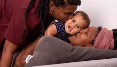 Two Black parents kiss their baby