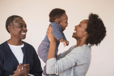 Young parent holds their baby with happy grandparent