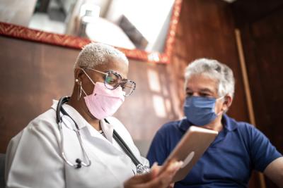 A doctor and patient wearing COVID-19 masks and looking at a tablet together.