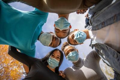 Young people wearing COVID masks link arms in a huddle