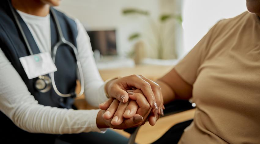 a home health aide holds the hand of an older woman
