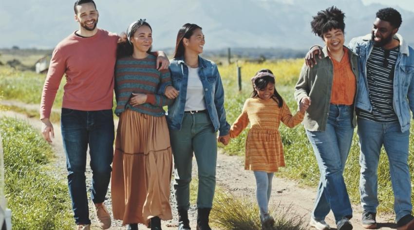 Five diverse adults and one child walk side by side through a field.