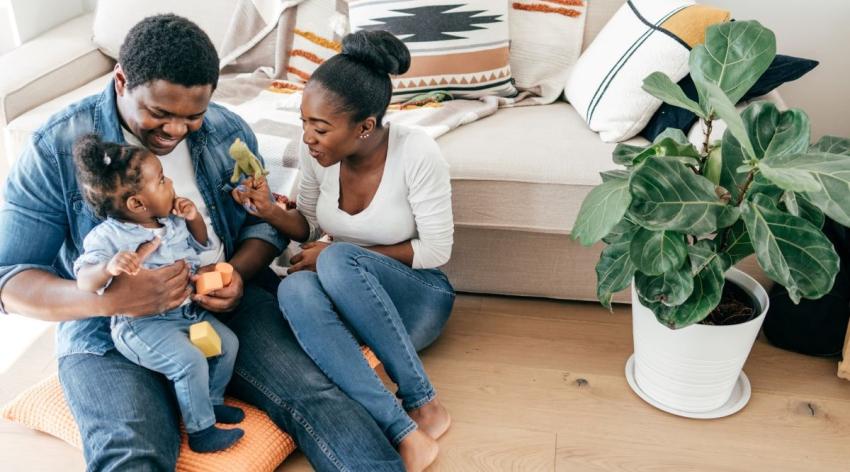 Happy Black mother and father with their small child playing on the floor with blocks and a stuffed toy.