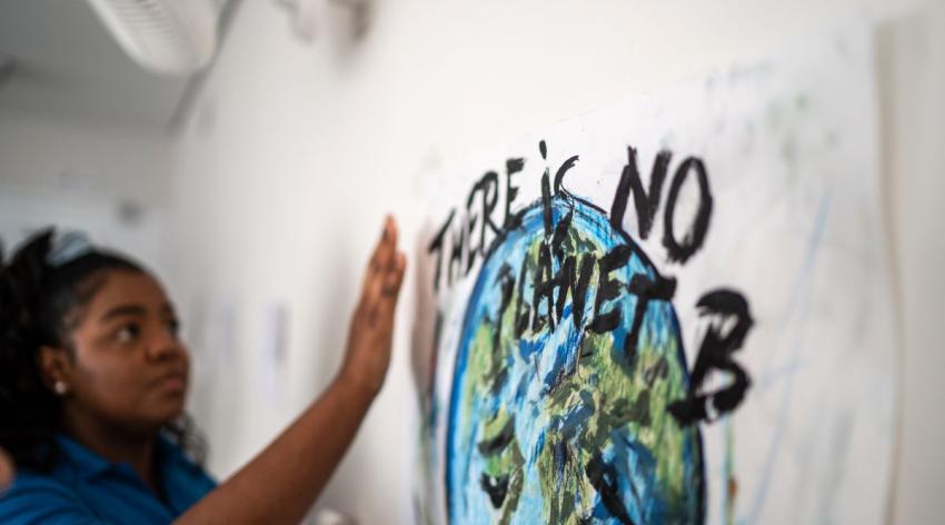 Young Black woman student hangs a poster that says "there is no planet B"