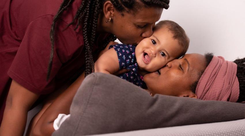 Two Black parents kiss their baby