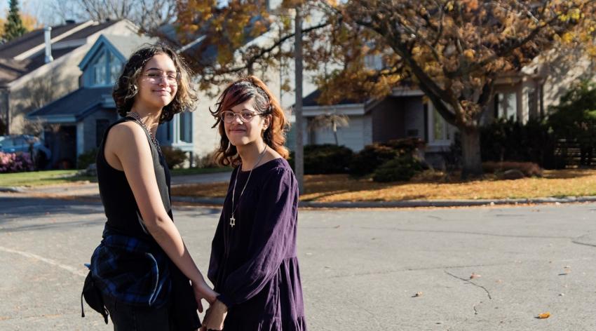 Portrait of a transgender girl and her non-binary teen friend walking in suburb street on a warm day in autumn. Both are multiracial, one half Asian, the other half Latina.