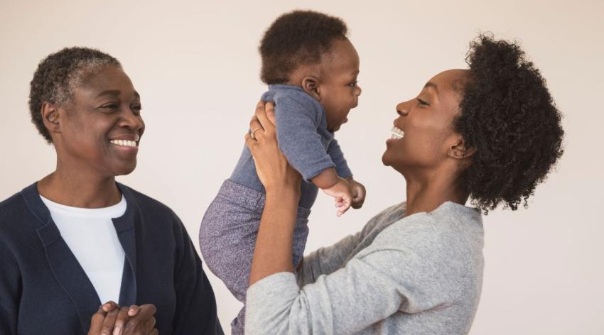 Young parent holds their baby with happy grandparent