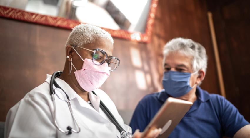 A doctor and patient wearing COVID-19 masks and looking at a tablet together.