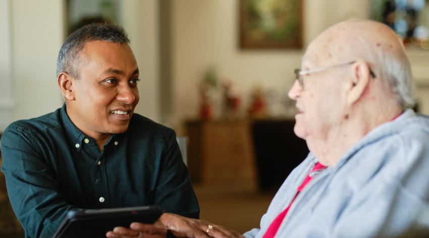 A caregiver holds the hand of an older man he's listening to.