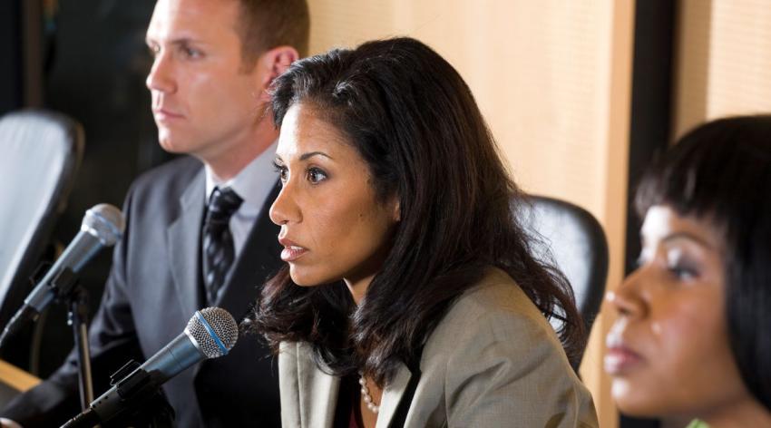 A group of city council persons sitting at a table with microphones listen closely at a hearing.