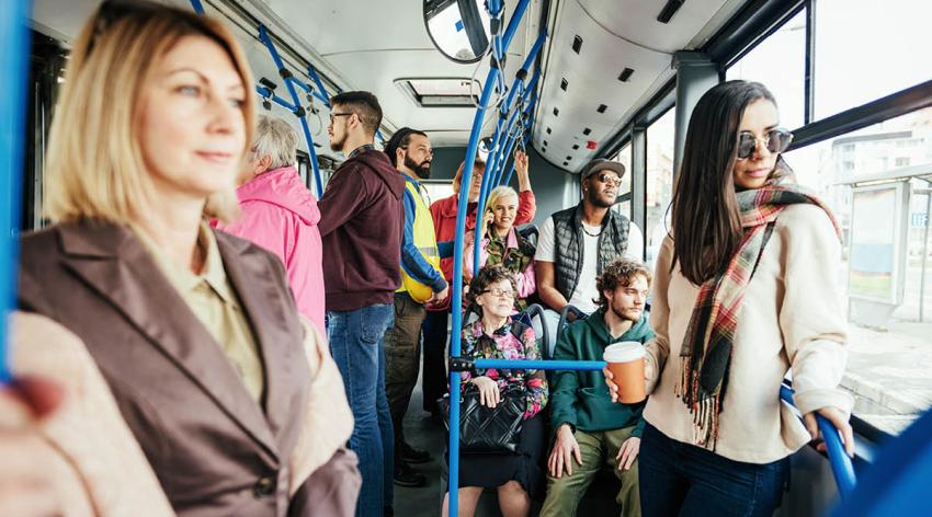 Many people riding a city bus, some sitting, some standing looking out the windows.