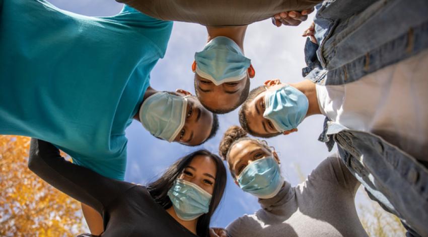 Young people wearing COVID masks link arms in a huddle